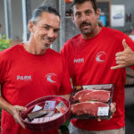 Two men in red shirts holding steak